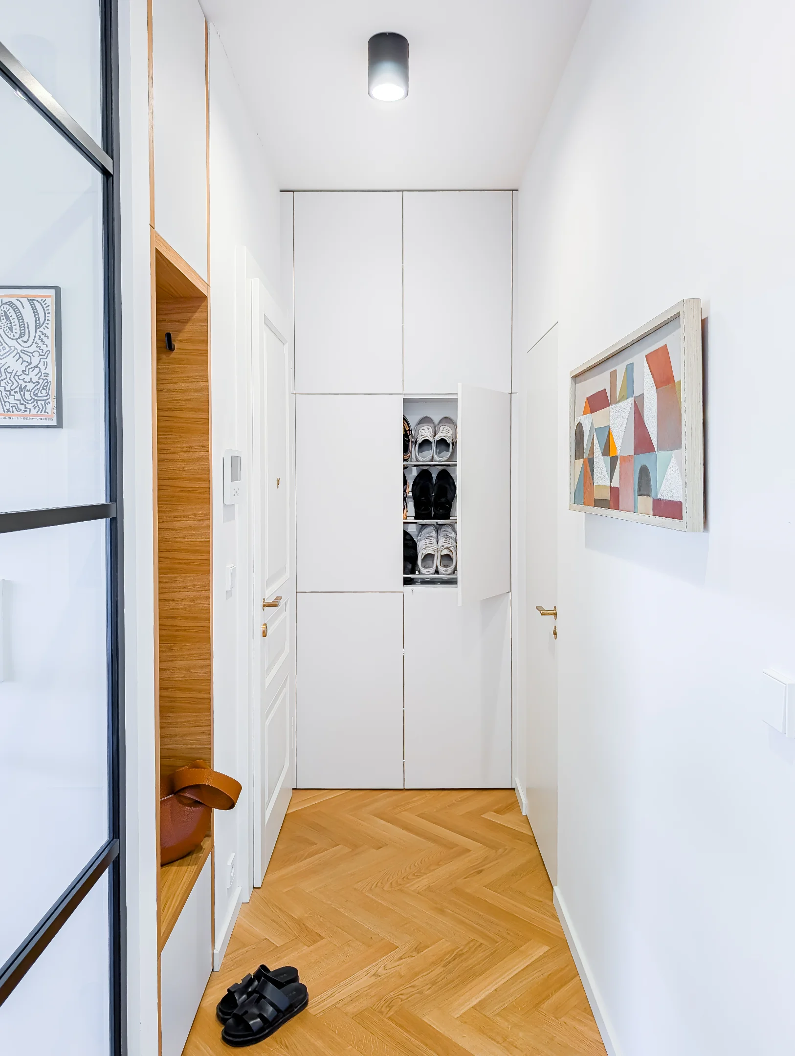 Moderní bílá chodba s dřevěnou podlahou a úložným prostorem.